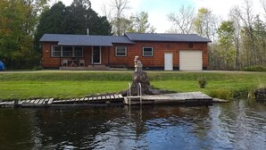 Ein Haus mit einem Steg, der in einen Teich führt, umgeben von einem grasbewachsenen Garten und Bäumen.
