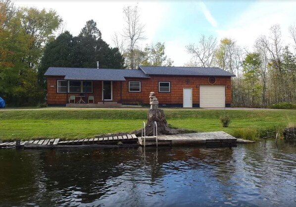 Una casa con un muelle que se adentra en un estanque, rodeada de césped y árboles.