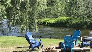 Eine Uferlandschaft mit blauen Adirondack-Stühlen und einem Holzstapel.