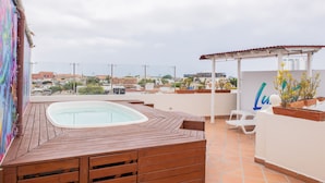 Eine Dachterrasse mit Whirlpool, Holzdeck, Blumentöpfen und einer Pergola.