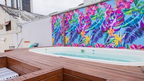 Eine Holzterrasse mit Whirlpool, umgeben von einem farbenfrohen tropischen Wandbild.