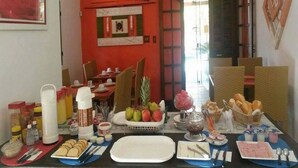Un comedor con una mesa preparada para el desayuno, que incluye frutas, bollería y bebidas.