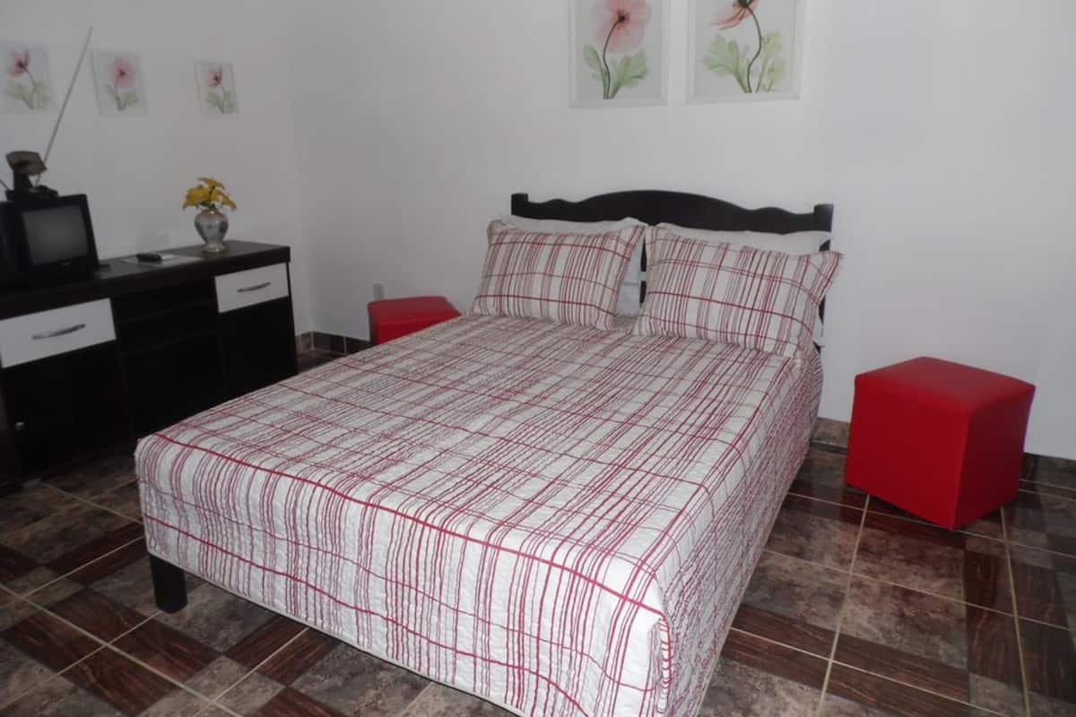 Une chambre à coucher avec un lit, une commode, un téléviseur et un tabouret rouge.