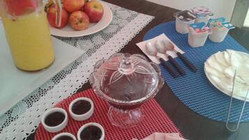 A table with a fruit plate, a pitcher of juice, a glass cake stand, small bowls of dip, and a plate of sliced meat.