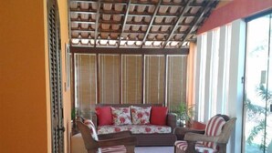 Un espacio de descanso al aire libre techado, con piso de madera, un sofá con cojines rojos y una silla.