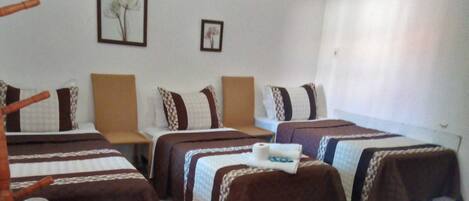 Una habitación de hotel con tres camas individuales, cada una con una colcha y almohadillas a rayas marrón y blanco a juego. Encima de las camas, hay un cuadro enmarcado en la pared.