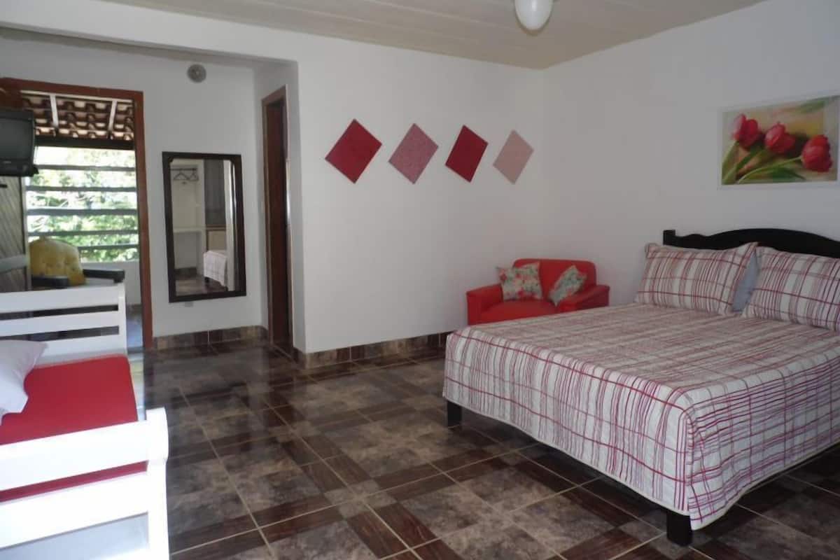 Une chambre à coucher avec un lit, un canapé rouge, un ventilateur de plafond et un tableau de fleurs accroché au mur.