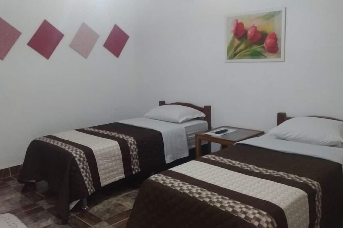 Une chambre avec deux lits simples, une petite table et un tableau représentant des tulipes accroché au mur.
