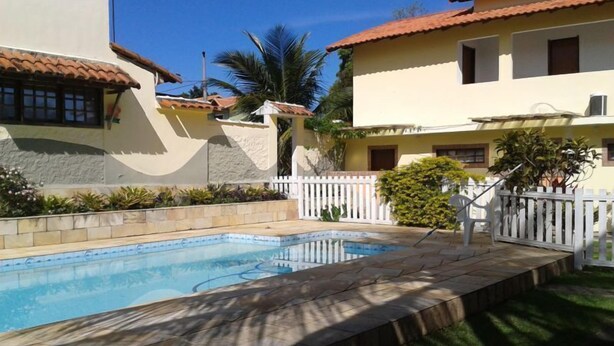 Una piscina con borde de piedra, rodeada por una valla blanca y vegetación.