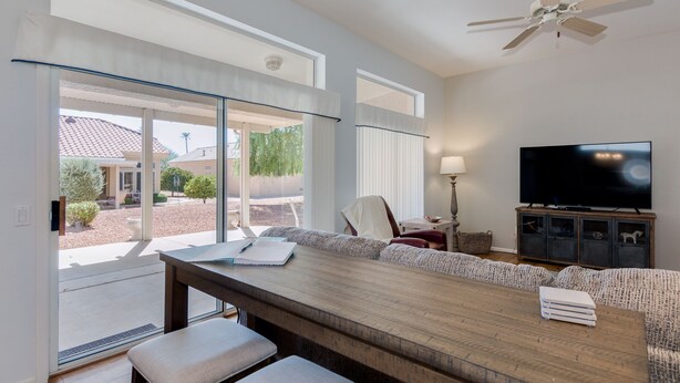 Un salon moderne doté d’une grande fenêtre, d’un ventilateur de plafond, d’un téléviseur à écran plat et d’une table basse en bois.