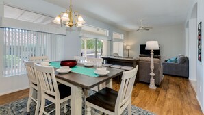 Un salon moderne avec un coin repas, agrémenté d’un lustre, d’un ventilateur de plafond et d’un téléviseur.