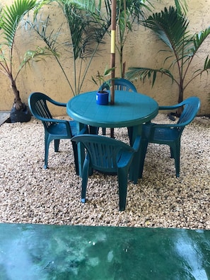 A round table with four chairs, surrounded by pebbles, with plants in the background. - Airport Sleepy Inn (Cancun)