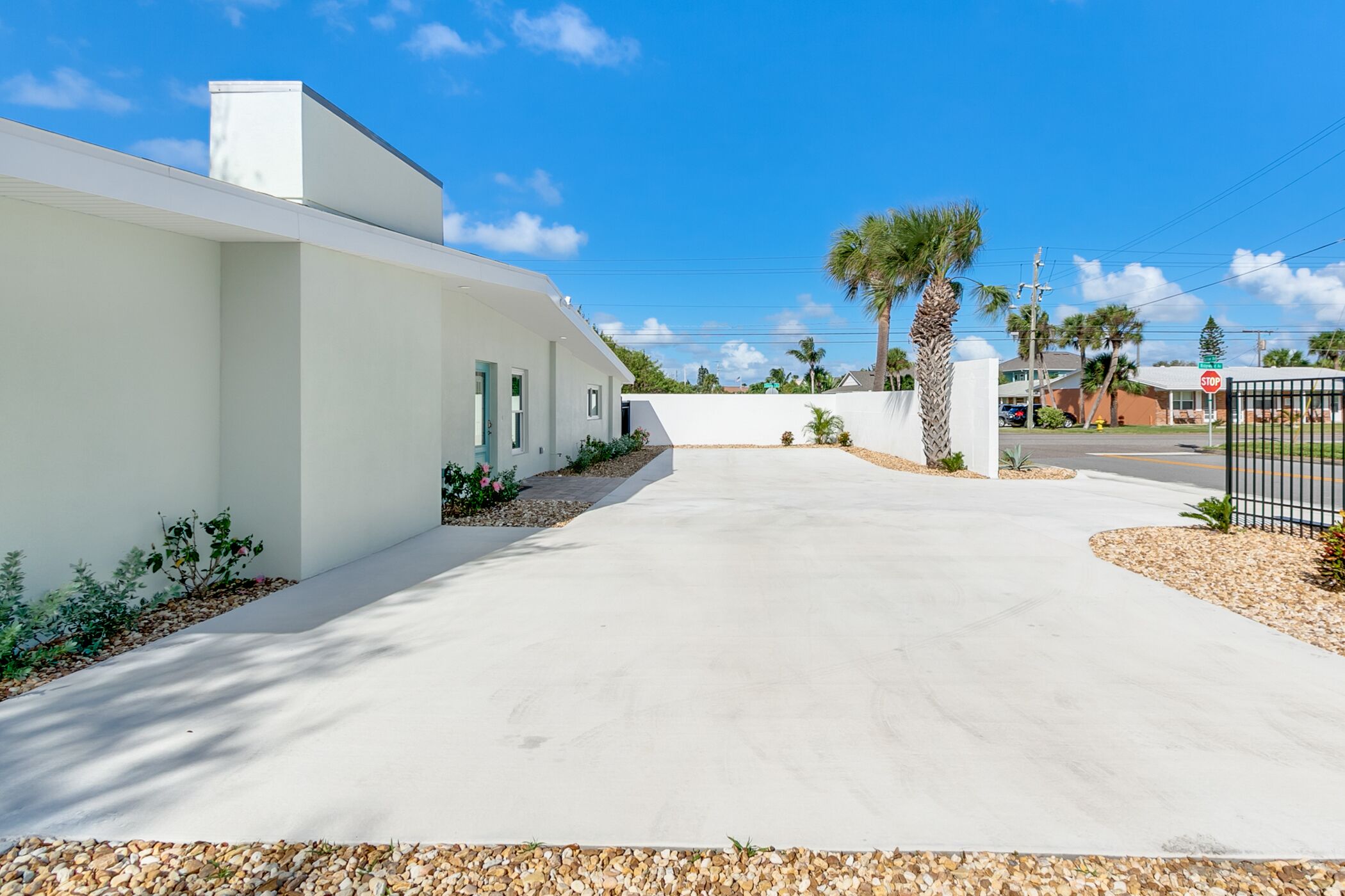 A modern white building with a concrete driveway, palm trees, and a stop sign in the background.