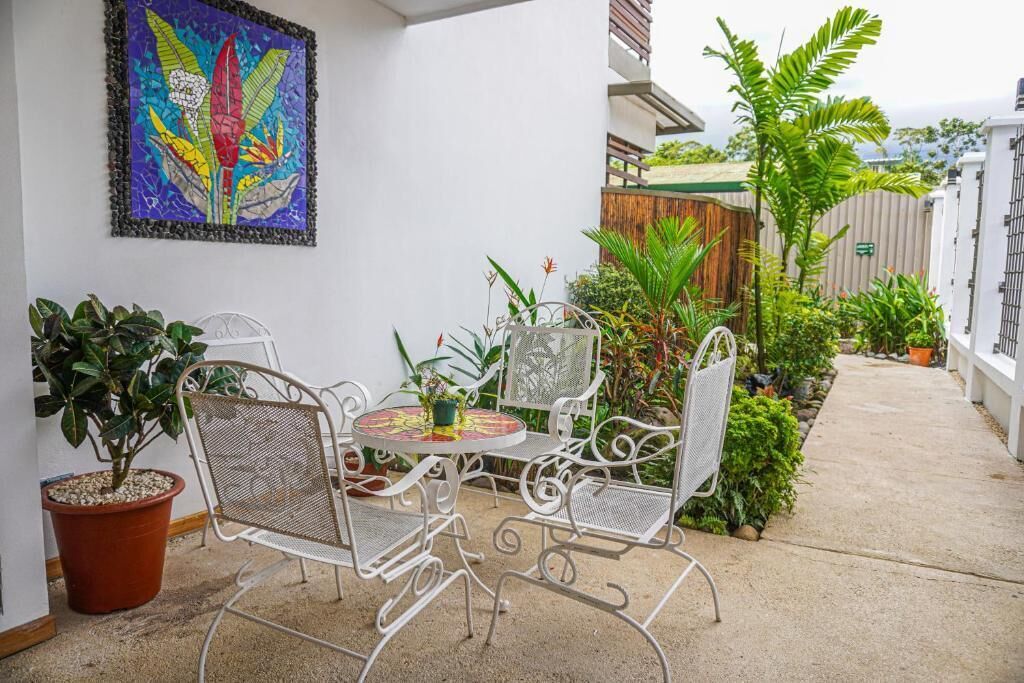 A patio with a metal table and chairs, surrounded by potted plants and a colorful artwork on the wall.
