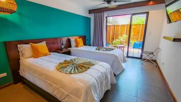 Habitación de hotel con dos camas, ventilador de techo, televisor y puerta corrediza de vidrio al exterior.