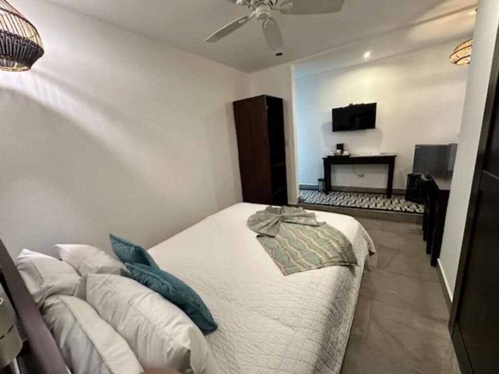 A bedroom with a bed, pillows, a ceiling fan, a TV, and a small table.