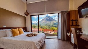 A hotel room with a bed, a desk, a TV, and a view of a mountain. - La Fortuna Lodge by Treebu Hotels (La Fortuna)
