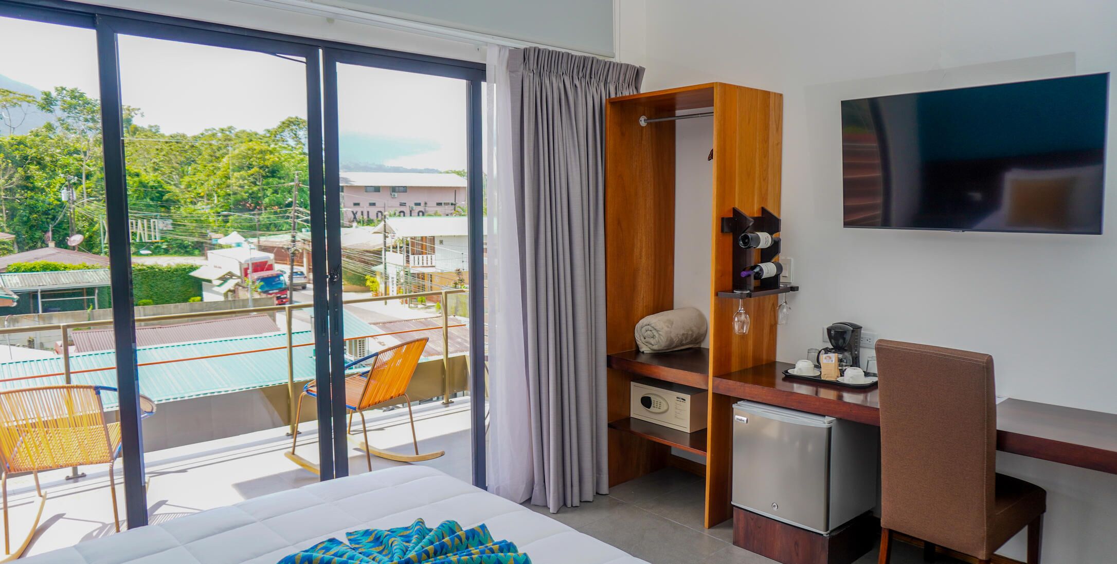 Habitación de hotel con balcón, una cama, escritorio con televisor y minibar.