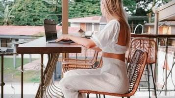 Una persona sentada a una mesa con una computadora portátil, bajo una estructura de techo de bambú.