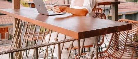 A person sitting at a wooden table with a laptop, under a thatched roof structure.