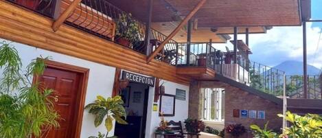 Zona de recepción con balcón de madera, plantas en macetas y un letrero que dice "RECEPCION".