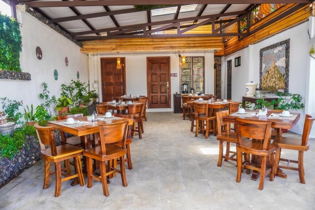 A restaurant with wooden tables and chairs, a stone floor, and a covered patio area with plants.