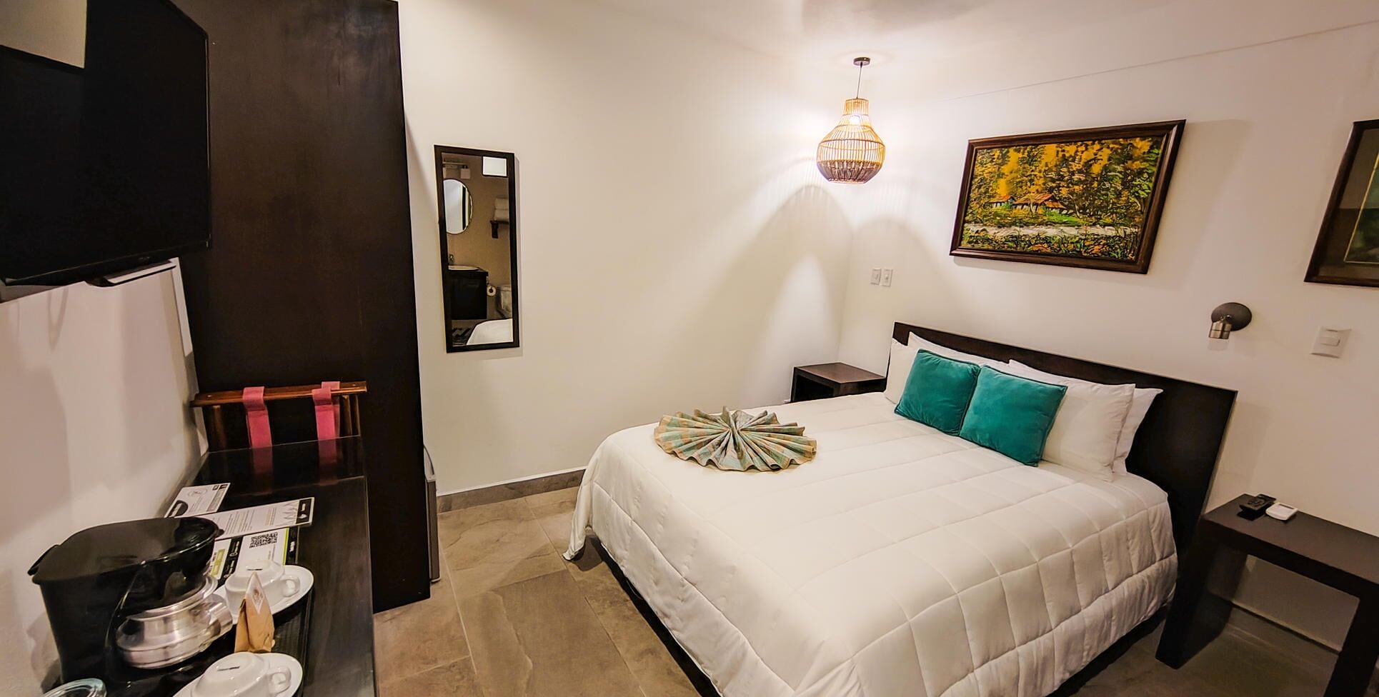 Une chambre d’hôtel avec un lit, une table de chevet, une lampe fixée au mur, un tableau et un miroir.
