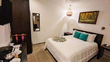 A hotel room with a bed, a nightstand, a wall-mounted lamp, a painting, and a mirror.