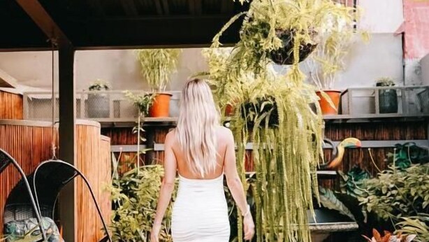 A woman walking on a concrete path in a garden area with various plants and a wooden fence. - La Fortuna Lodge by Treebu Hotels (La Fortuna)