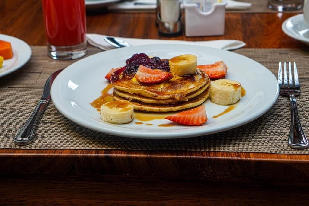 Un plato de desayuno con tortitas, fresas, plátanos y bayas.