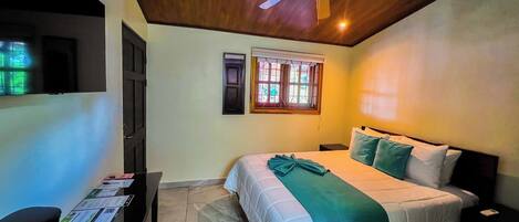 Un dormitorio con cama, ventilador de techo, ventana con contraventanas y escritorio con una bandeja de objetos.