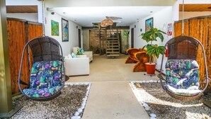 A modern interior with two hanging chairs, a white sofa, and a staircase leading to a loft area. - La Fortuna Lodge by Treebu Hotels (La Fortuna)
