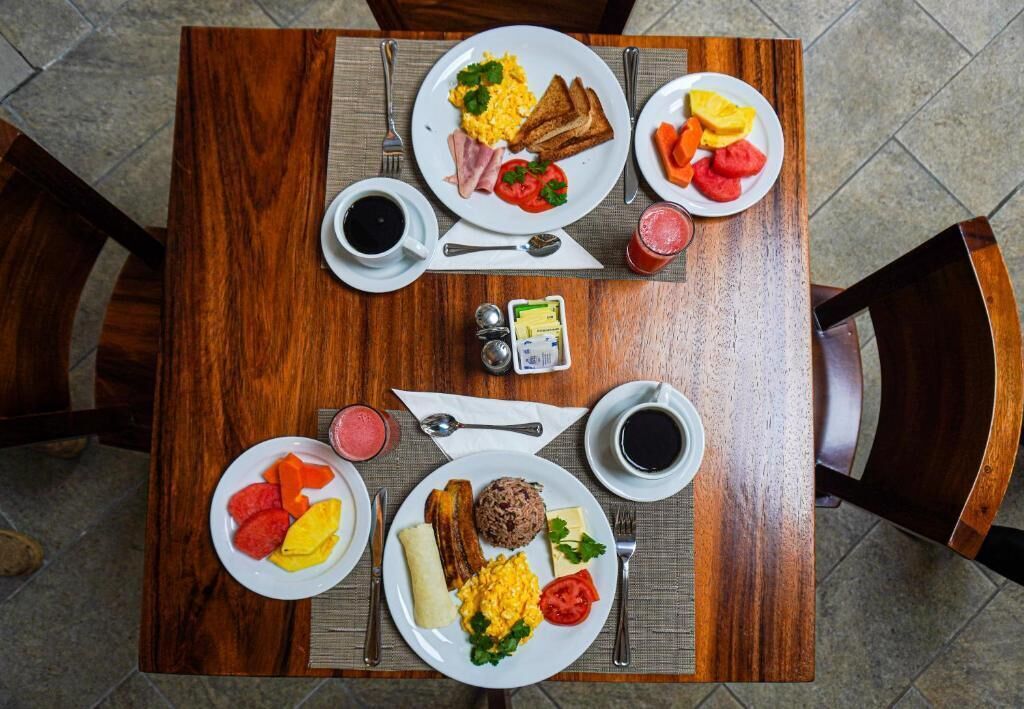 A wooden dining table with plates of breakfast food, cups of coffee, and condiments.