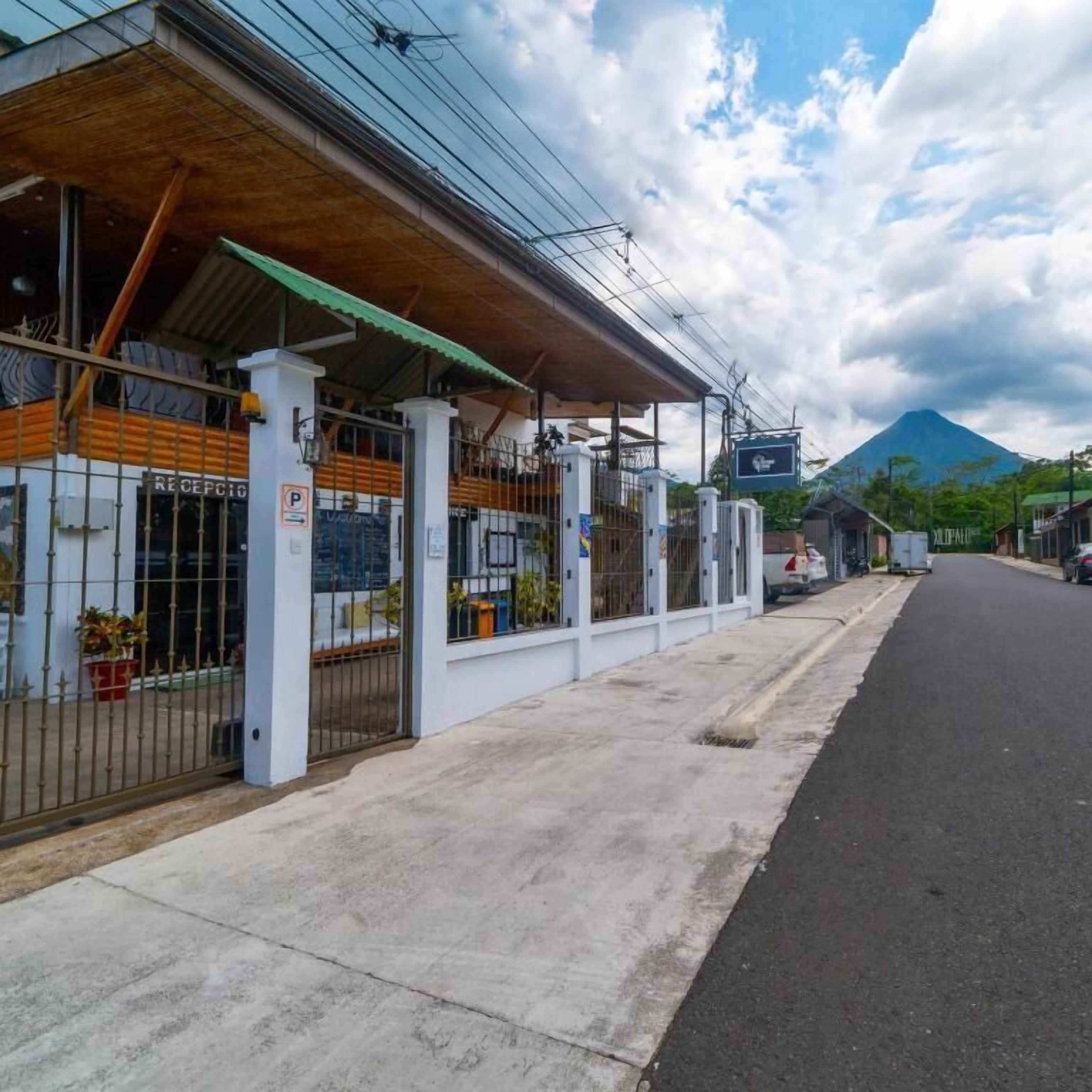 A building with a covered entrance, a gated parking area, and a view of a mountain in the background.