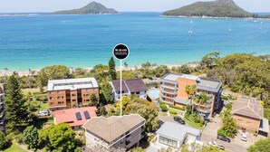 A coastal hotel with multiple buildings, a swimming pool, and a view of the ocean and nearby islands.