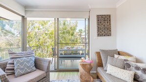 A modern living room with a balcony, wicker furniture, and a view of trees.