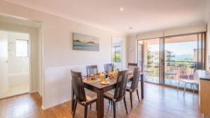 A dining area with a table set for four, a painting on the wall, and a view of the sea through large windows.