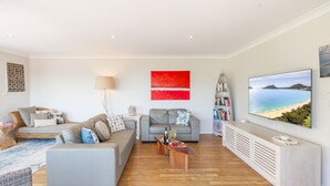 A modern living room with a grey sofa, a coffee table, a bookshelf, and a TV displaying a beach scene.
