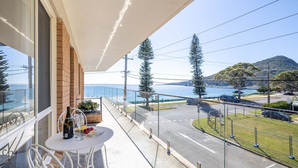 Ein Balkon mit Esstisch, der auf eine Küstenstraße mit Verkehr und Grünflächen blickt.