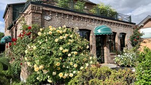 Ein Backstein-Landhaus mit einem grünen Vordach, einem Rosenbusch und einem Schild, auf dem 'Rose Cottage' steht.
