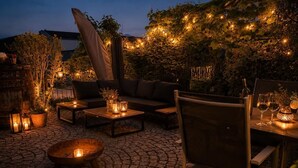 Eine Terrassengruppe im Freien mit Steinplattenboden, einer Couch, einem Esstisch und stimmungsvoller Beleuchtung.