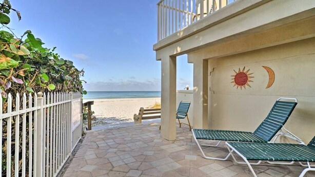 Eine Terrasse direkt am Strand mit Liegestühlen, einem weißen Zaun und einem Wandbild von Sonne und Mond.