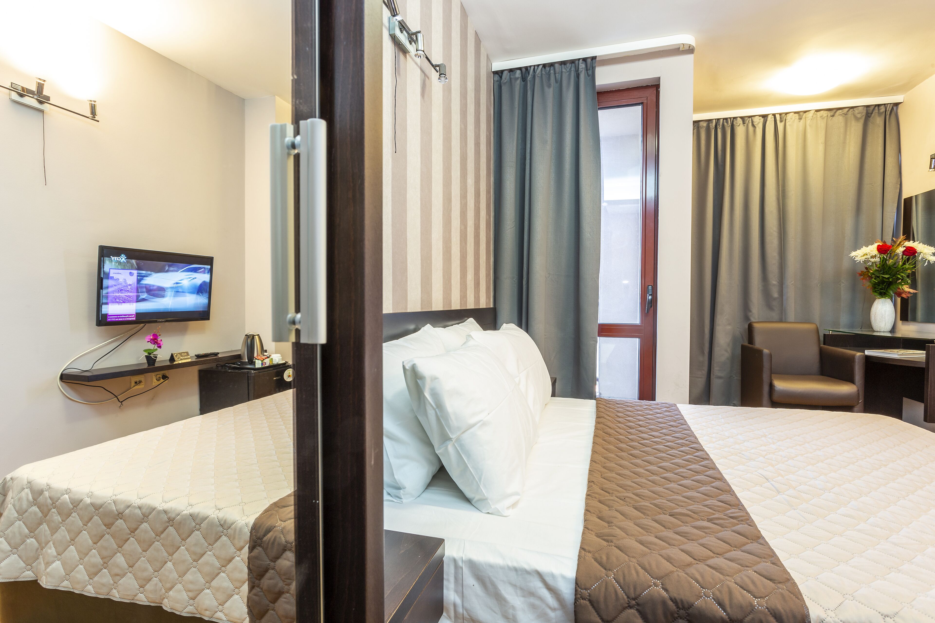 A hotel room with a bed, a desk, a chair, a television, and a window with curtains.