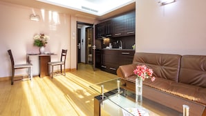 A modern living room with a glass coffee table, a brown leather sofa, and a dining area with two chairs and a small table. - CityHome Aparthotel (Sofia)