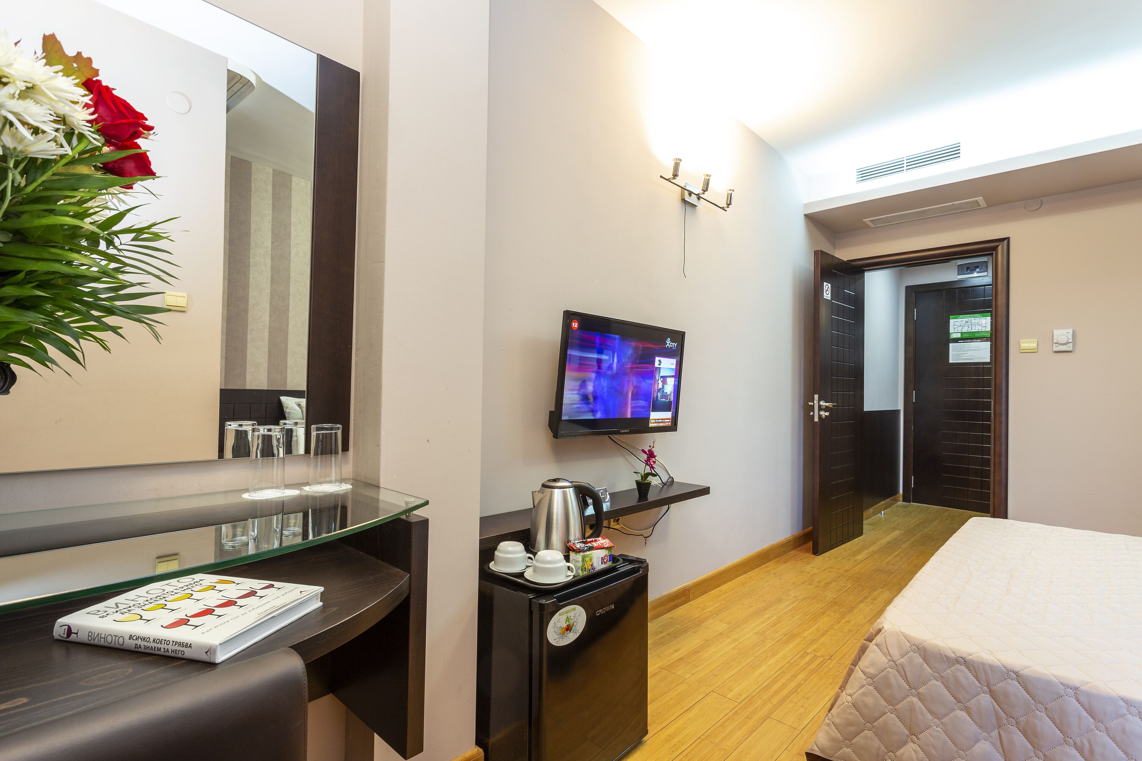 A hotel room with a bed, a desk with a coffee maker, a TV, and a mirror.