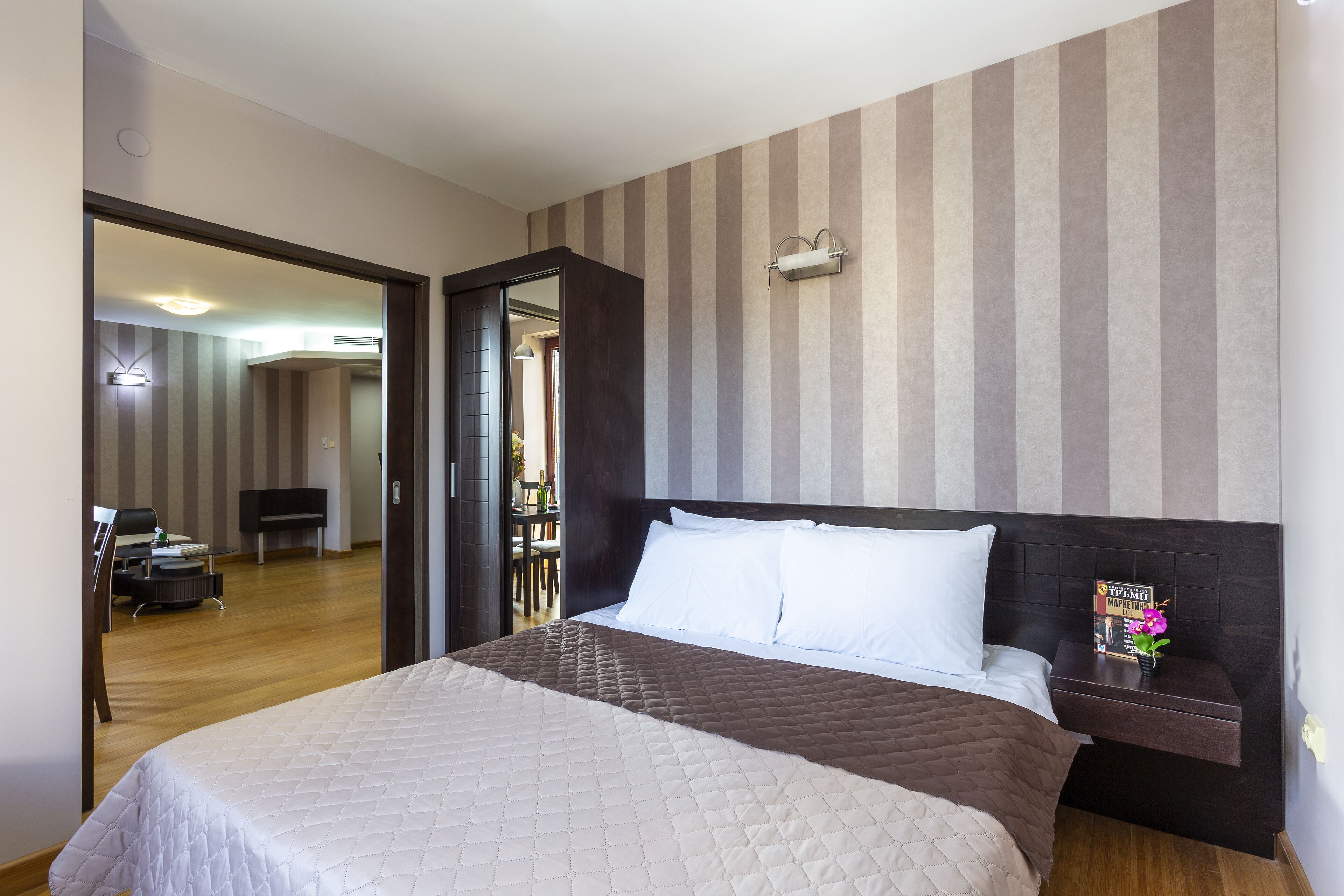 Quarto de hotel com uma cama grande, mesa de cabeceira, espelho e parede listrada.
