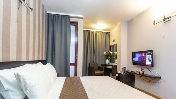 A hotel room with a large bed, a desk with a computer, a TV, and a chair. - CityHome Aparthotel (Sofia)