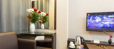 A hotel room with a sofa, a glass table with a vase of flowers, a television, and a coffee machine.