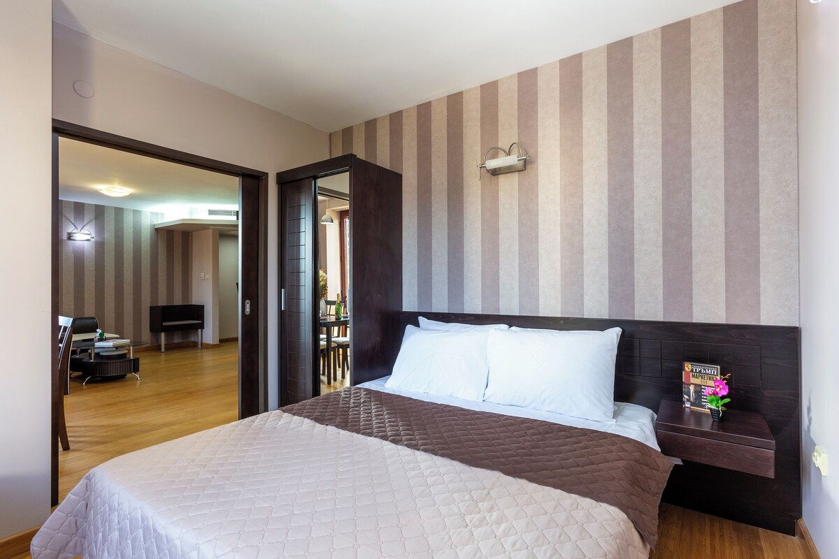 A hotel room with a large bed, a nightstand, a mirror, and a striped wall.