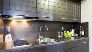 A modern kitchen with a stainless steel sink, a built-in induction cooktop, and a kettle. There are two bottles of wine and a bowl of green apples on the counter. - CityHome Aparthotel (Sofia)